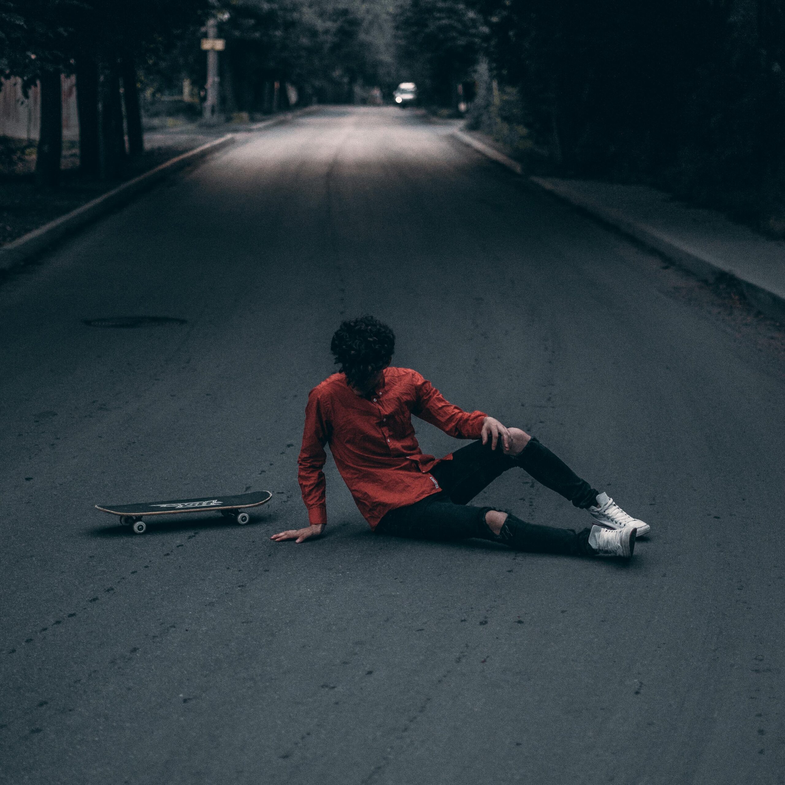 A skateboarder in casual wear sits on a deserted street, evoking a moody atmosphere.