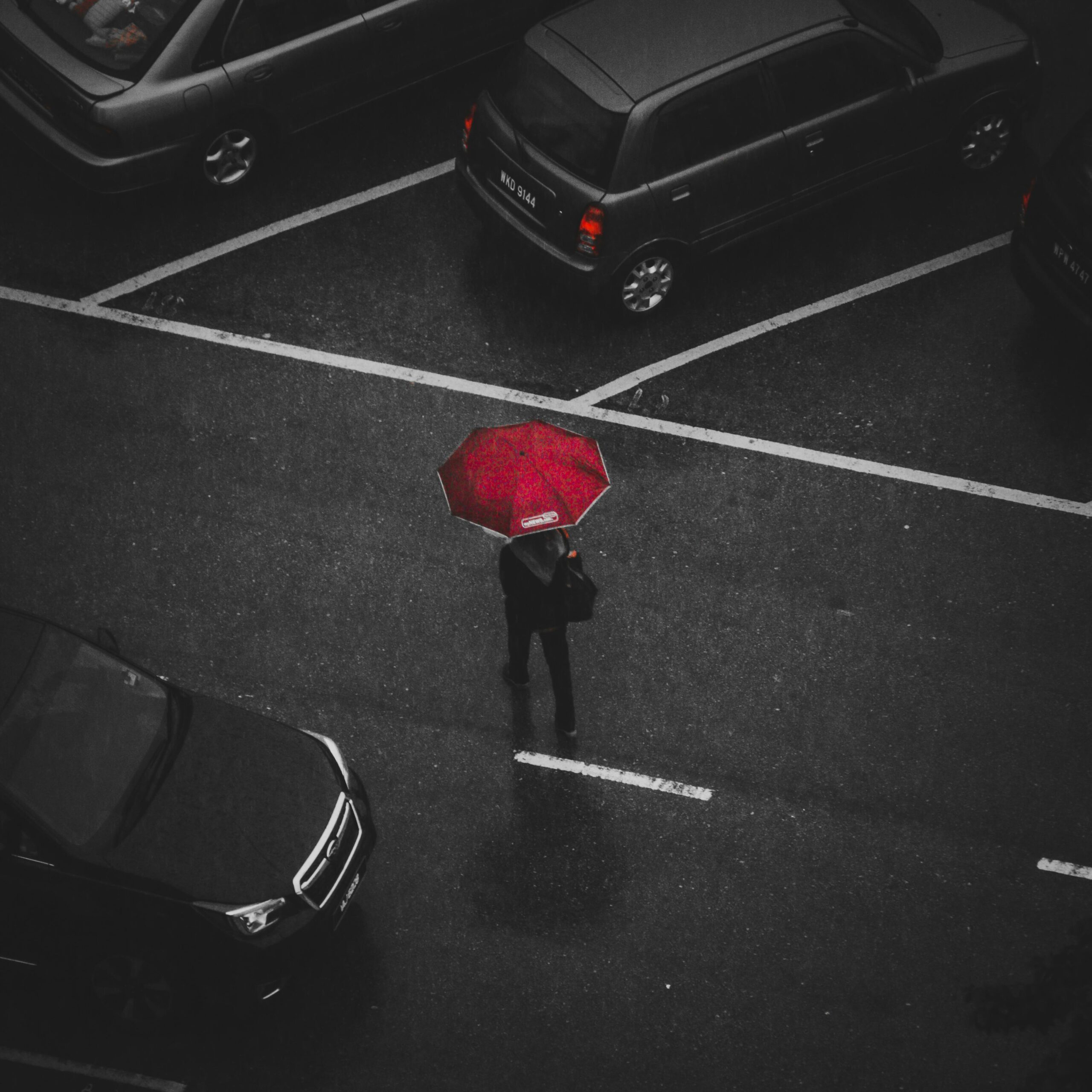 Top view of a person with a red umbrella walking in a rainy parking lot.